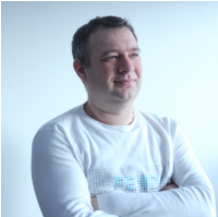 A man in a white long-sleeve shirt glancing to the side against a light blue background.